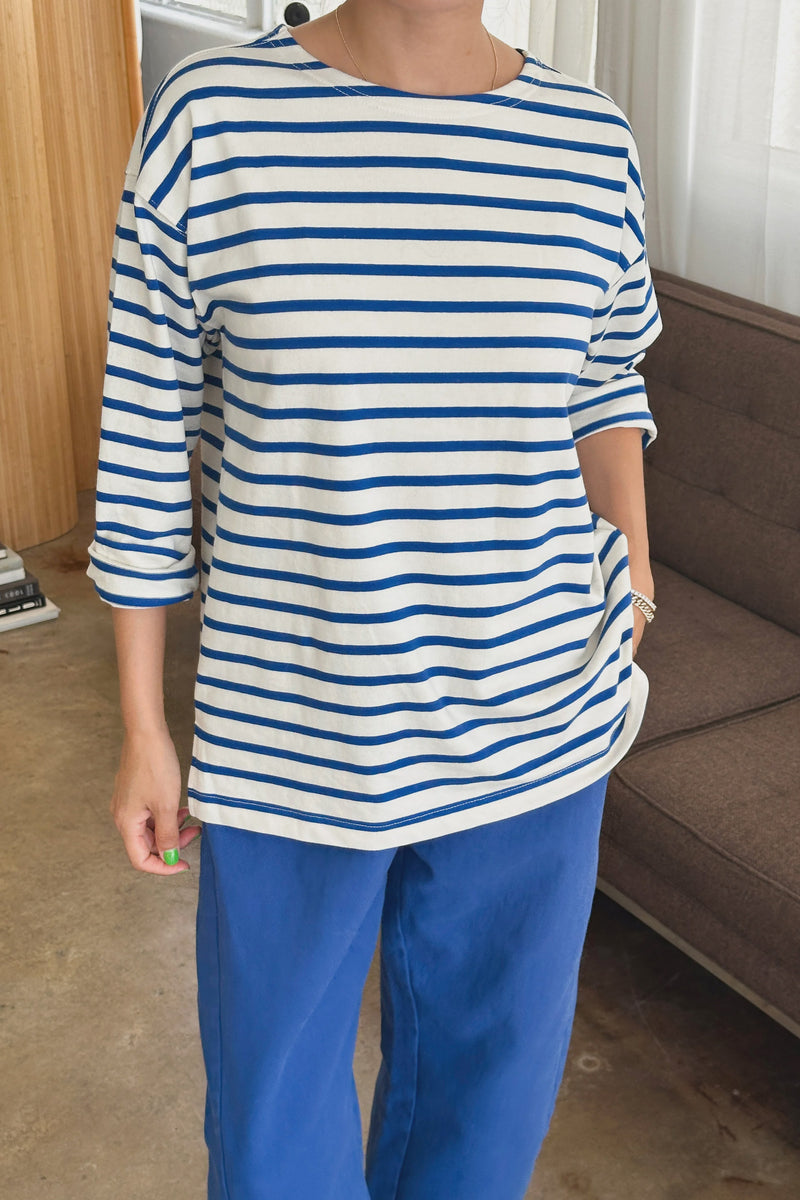 Person wearing a blue and white striped shirt and blue pants in a room with a couch and window.