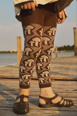 Person wearing brown leggings with mushroom pattern on a wooden dock by a body of water.
