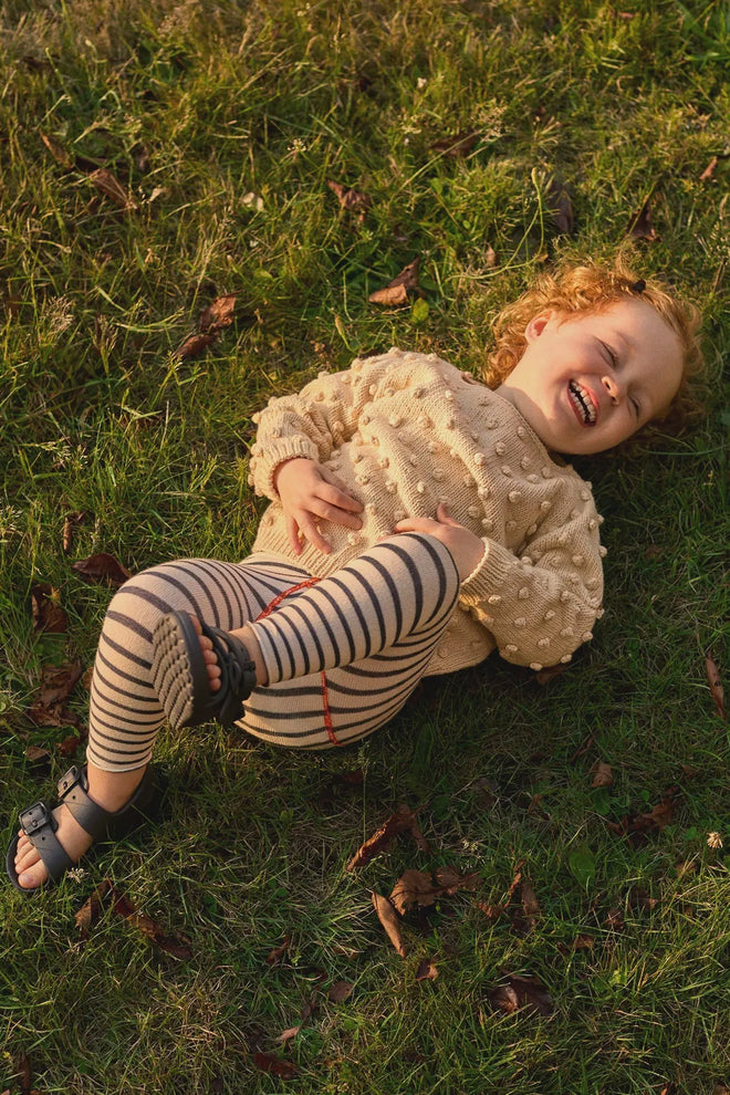 Child lying on grass wearing a beige sweater and striped leggings.