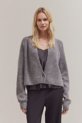 Woman wearing a gray cardigan over a dark top and pants on a plain background