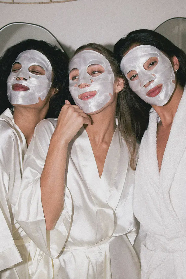 Three women in white robes and face masks posing together.