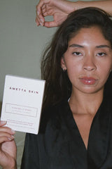 Woman holding a 'Ametta Skin' product packaging against a neutral background
