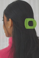 Person with a green hair clip in their dark hair against a white curtain background