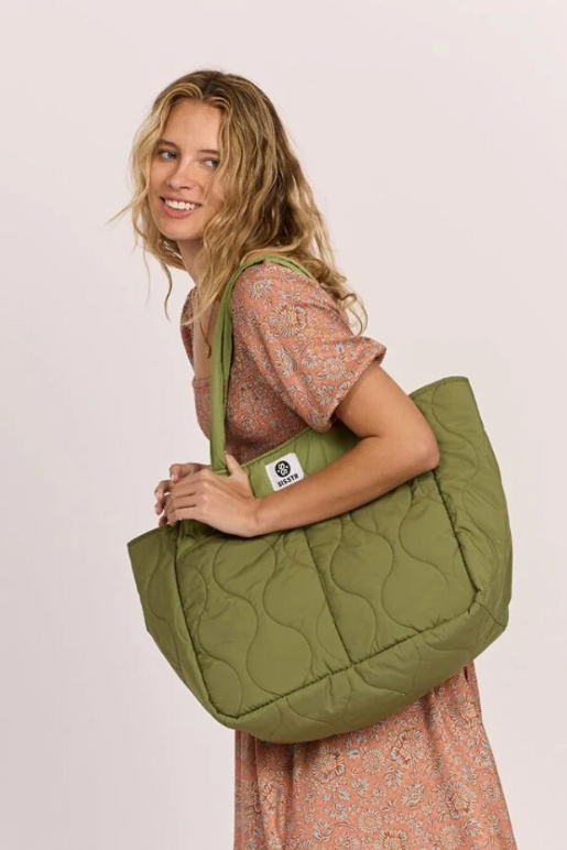 Woman holding a green quilted bag against a plain background