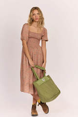 Woman holding a green bag wearing a patterned dress on a white background