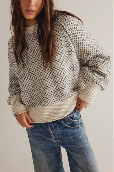 Person wearing a patterned sweater and jeans against a plain background