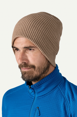 Man wearing a beige knit beanie and blue jacket on a white background