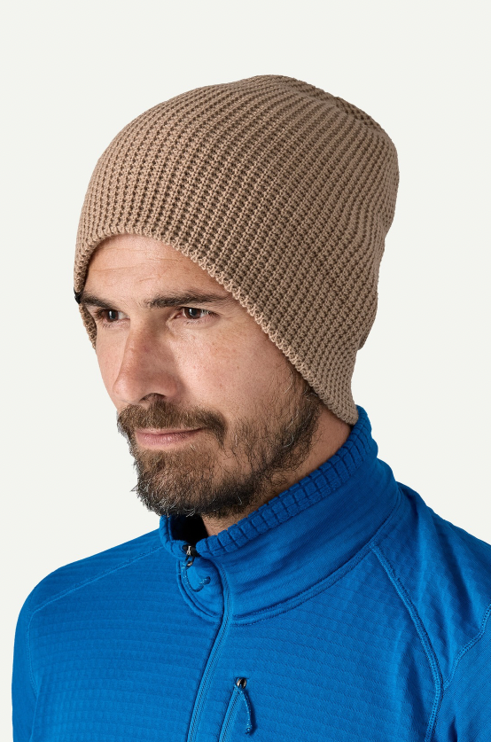 Man wearing a beige knit beanie and blue jacket on a white background