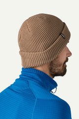 Man wearing a brown knit beanie and blue jacket on a white background