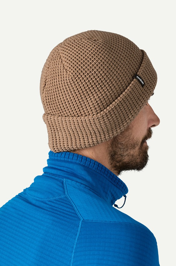 Man wearing a brown knit beanie and blue jacket on a white background
