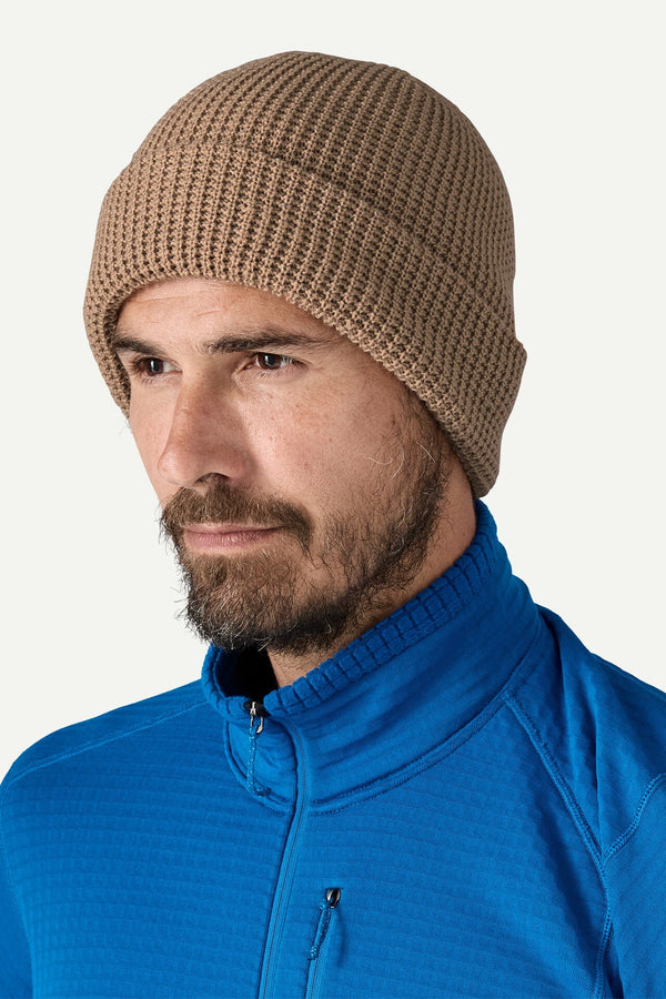 Man wearing a brown knit beanie and blue pullover on a white background