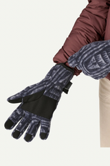 Person wearing patterned gloves and a brown jacket on a white background