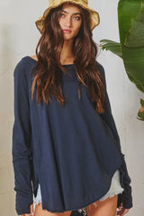 Woman wearing a navy blue long-sleeve top with a white background and green plants.