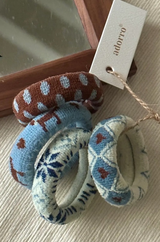 Decorative hairties with a pattern on a textured surface, with a brand tag visible.