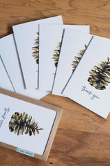 Set of greeting cards with pine cone design and 'Thank you' text on a wooden surface