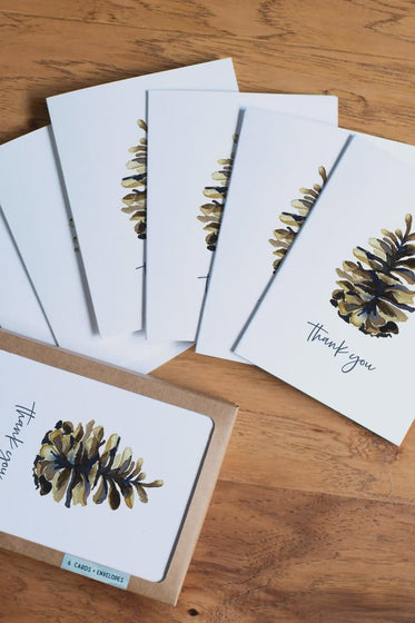 Set of greeting cards with pine cone design and 'Thank you' text on a wooden surface