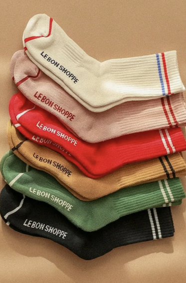 A stack of various colored socks with the text 'LE BON SHOPPE' on the side, including colors red, beige, green, black, and white.
